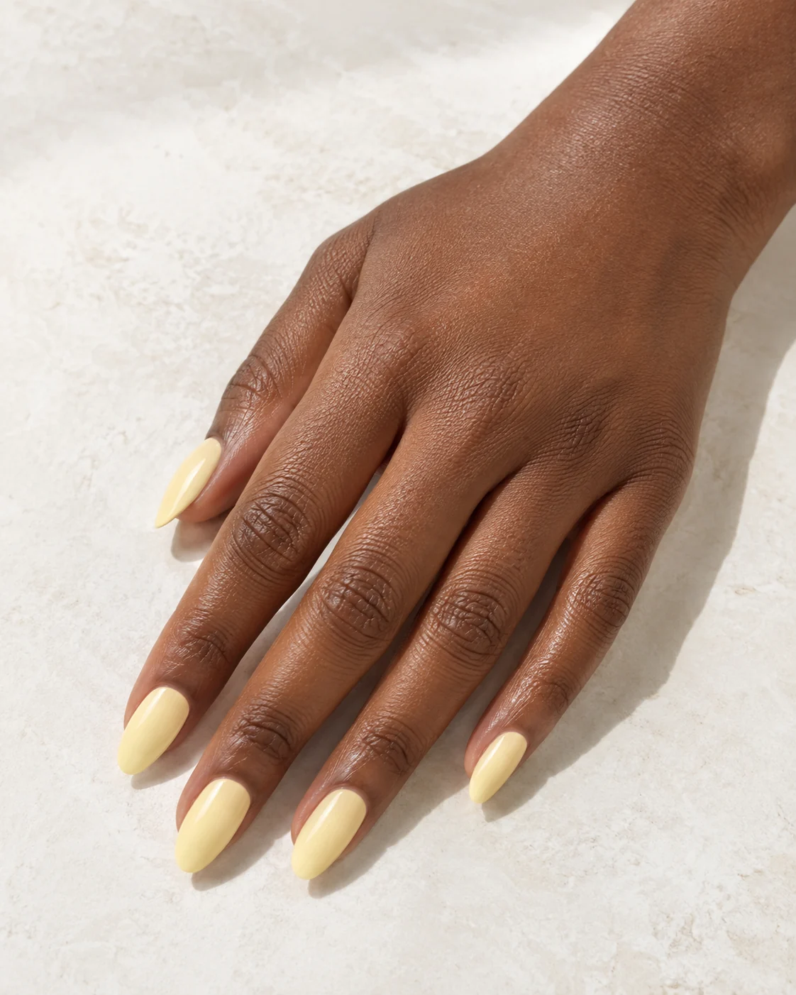 Soft butter-yellow polish on almond-shaped nails